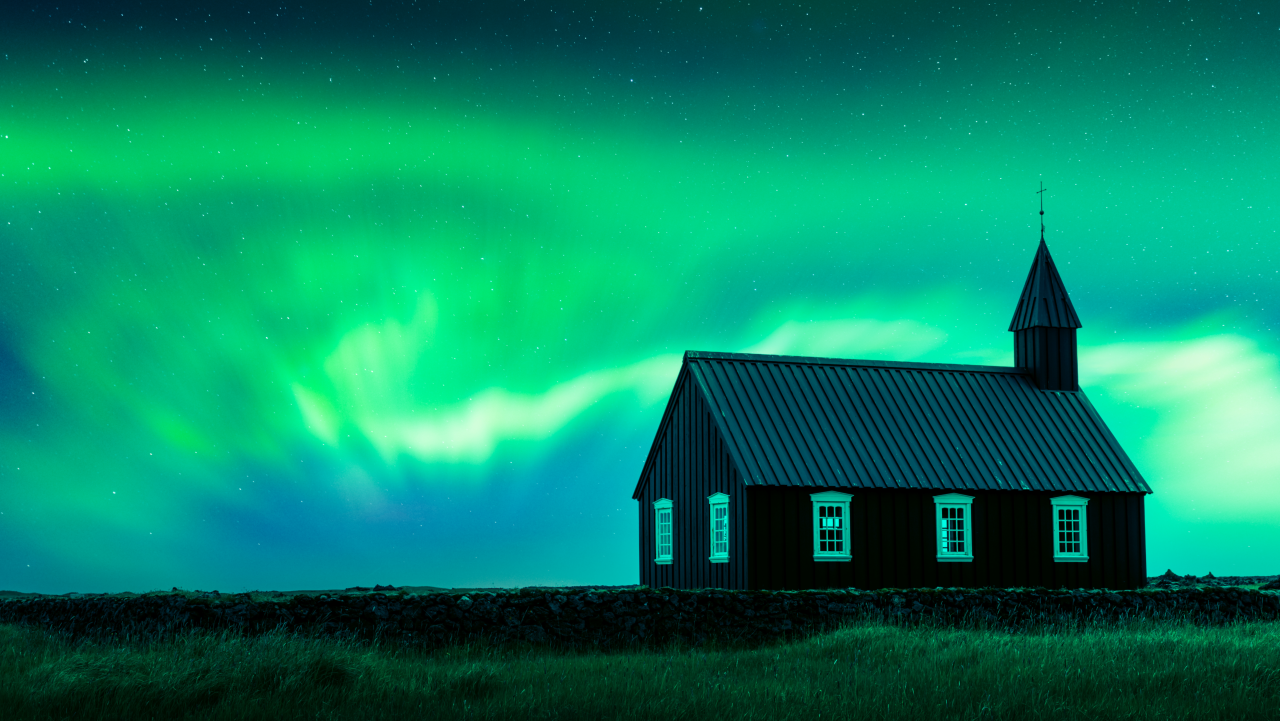 Aurora boreal verde sobre una iglesia negra tradicional en Islandia durante una noche estrellada.